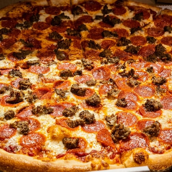 A large pizza with pepperoni and sausage toppings, half of it sliced, in a cardboard box.