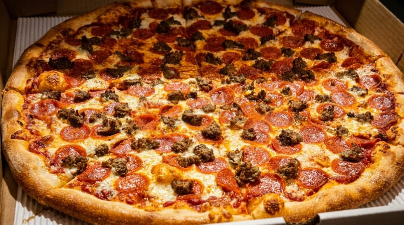 A large pizza with pepperoni and sausage toppings, half of it sliced, in a cardboard box.
