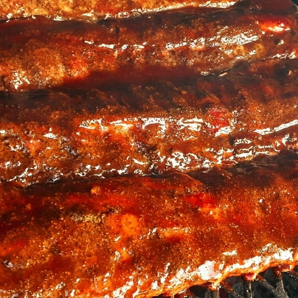 Four racks of ribs covered in a thick, glistening barbecue sauce on a grill.