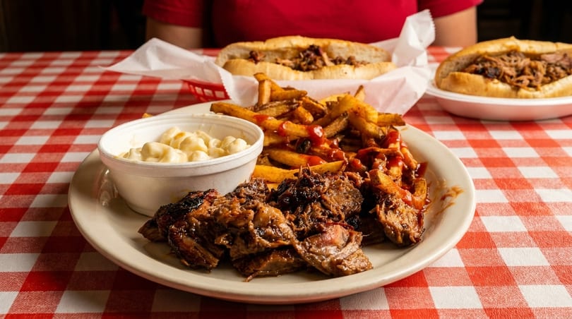 Barbecue plate with brisket, fries, mac and cheese, and two pulled pork sandwiches on a red checkered tablecloth.