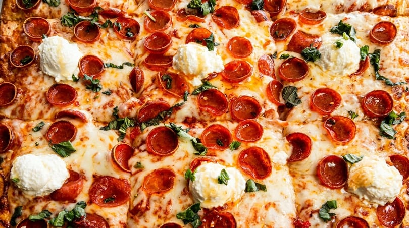 Close-up of a pepperoni pizza with dollops of ricotta cheese and fresh basil.